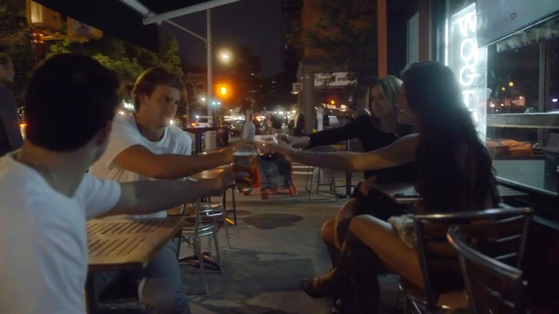 Friends raising their drinks around a sidewalk table